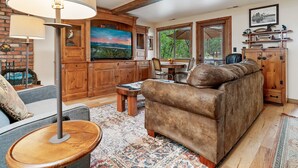 Un salon chaleureux avec une grande télévision, des meubles en bois et une vue par la fenêtre.