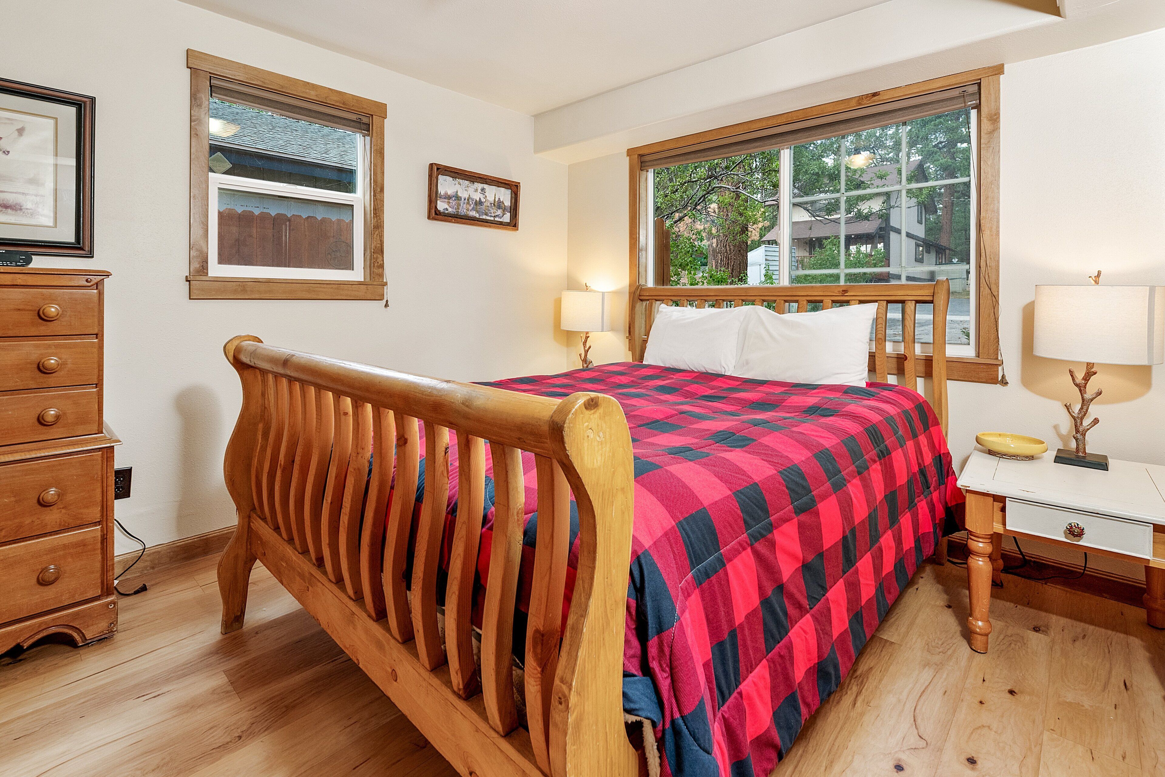 Un lit en bois avec une couvre-lit à carreaux, une table de chevet avec une lampe et une commode avec des tiroirs.