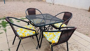 Une terrasse avec une table en métal et des chaises en osier, agrémentées de coussins à motifs de citron.
