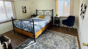 Une chambre à coucher comprenant un lit, un bureau, une chaise, un ventilateur de plafond et une fenêtre avec des stores.