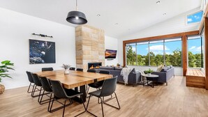 Uma sala de estar moderna com uma mesa de jantar de madeira, cadeiras pretas, um sofá cinza e uma lareira.