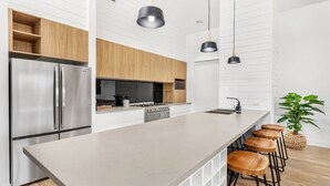 Cozinha moderna com uma ilha grande, eletrodomésticos de aço inoxidável, armários de madeira e iluminação pendente.