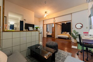 A modern hotel room with a glass coffee table, a sofa, a desk with a chair, a bed with a wooden headboard, a large mirror, and a potted plant. - MIYAKOJIMA Upuyu (Miyakojima)