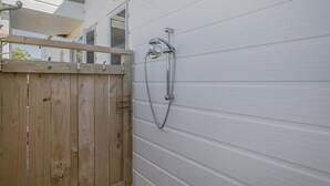 Um portão de madeira que dá para uma casa com chuveiro de metal fixado na parede externa.