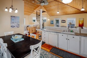 A kitchen with white cabinets, a wooden dining table, and a built-in dishwasher.