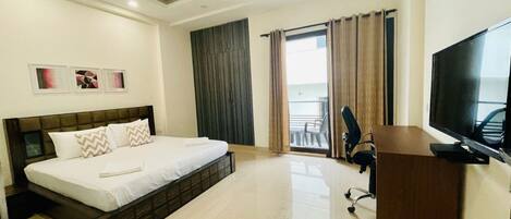 A hotel room with a bed, a desk, a chair, a TV, and a balcony with curtains.