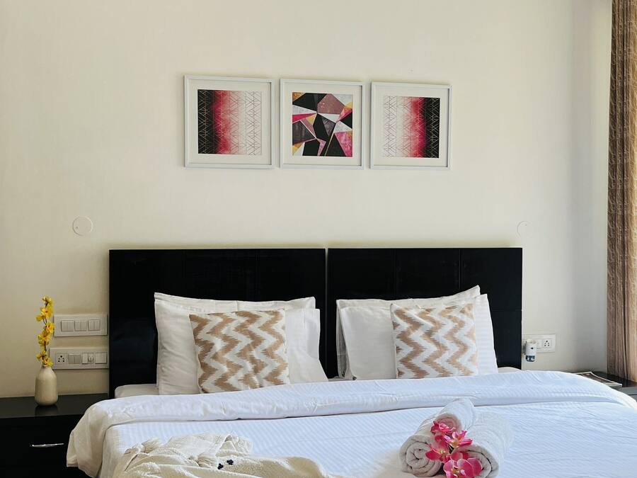 A neatly made bed with a white comforter and a blanket with bear faces, a black headboard, and three abstract art pieces on the wall.