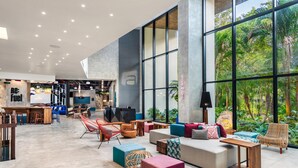 A spacious lobby with a large seating area, a reception desk, and a view of lush greenery through large windows. - Aloft Tulum (Tulum)