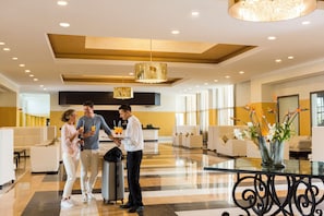 Un vestíbulo de hotel con una recepción, zonas de estar y una mesa de cristal con jarrones.