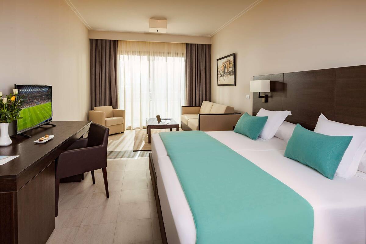 Una habitación de hotel con una cama grande, un escritorio, una silla, un televisor y una ventana con cortinas.