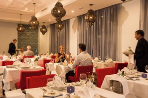 Un restaurante con mesas redondas, sillas rojas y lámparas colgantes decorativas.