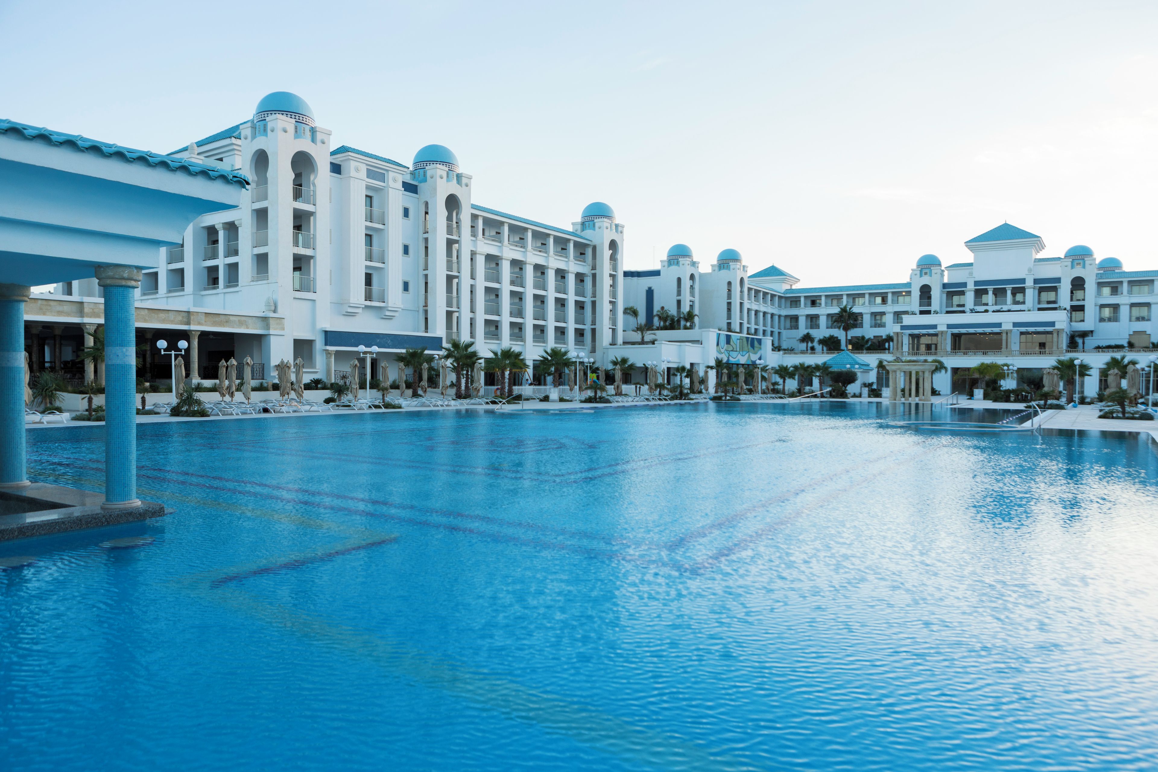 A large swimming pool with a modern hotel in the background.