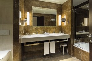 Une salle de bain moderne dotée d’un meuble-lavabo à deux vasques, d’un grand miroir, d’une douchette à main et d’une baignoire séparée.