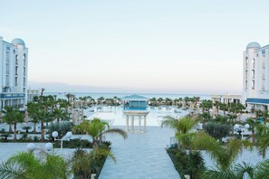 Un complexe hôtelier doté d’une piscine centrale, de palmiers et offrant une vue sur la mer.