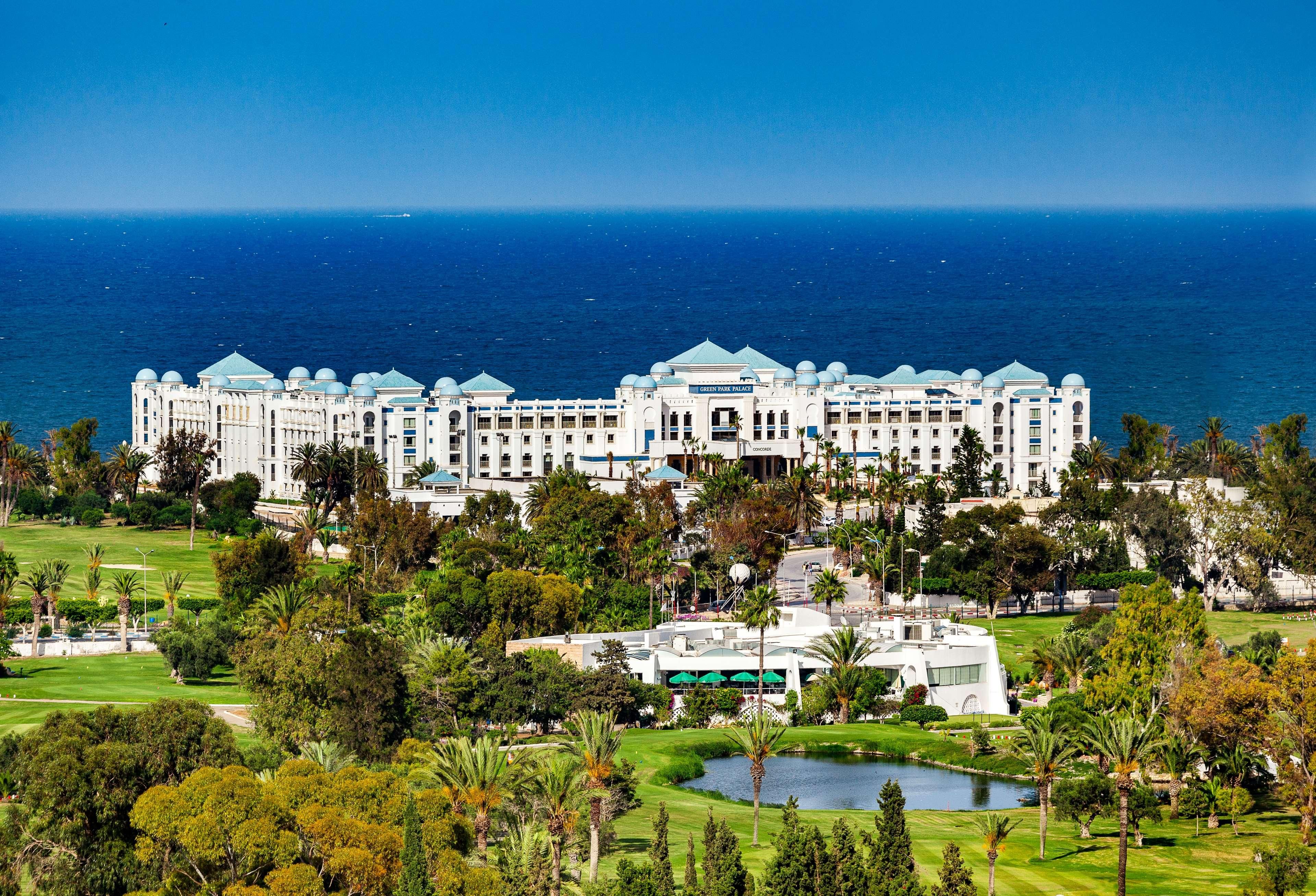 A large, white hotel with multiple domed roofs, a golf course, and a body of water in the foreground.