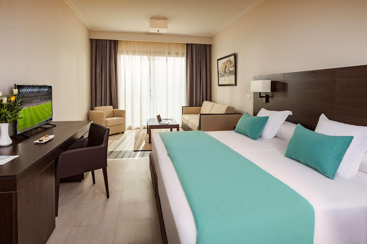 A hotel room with a large bed, a desk, a chair, a television, and a window with curtains.