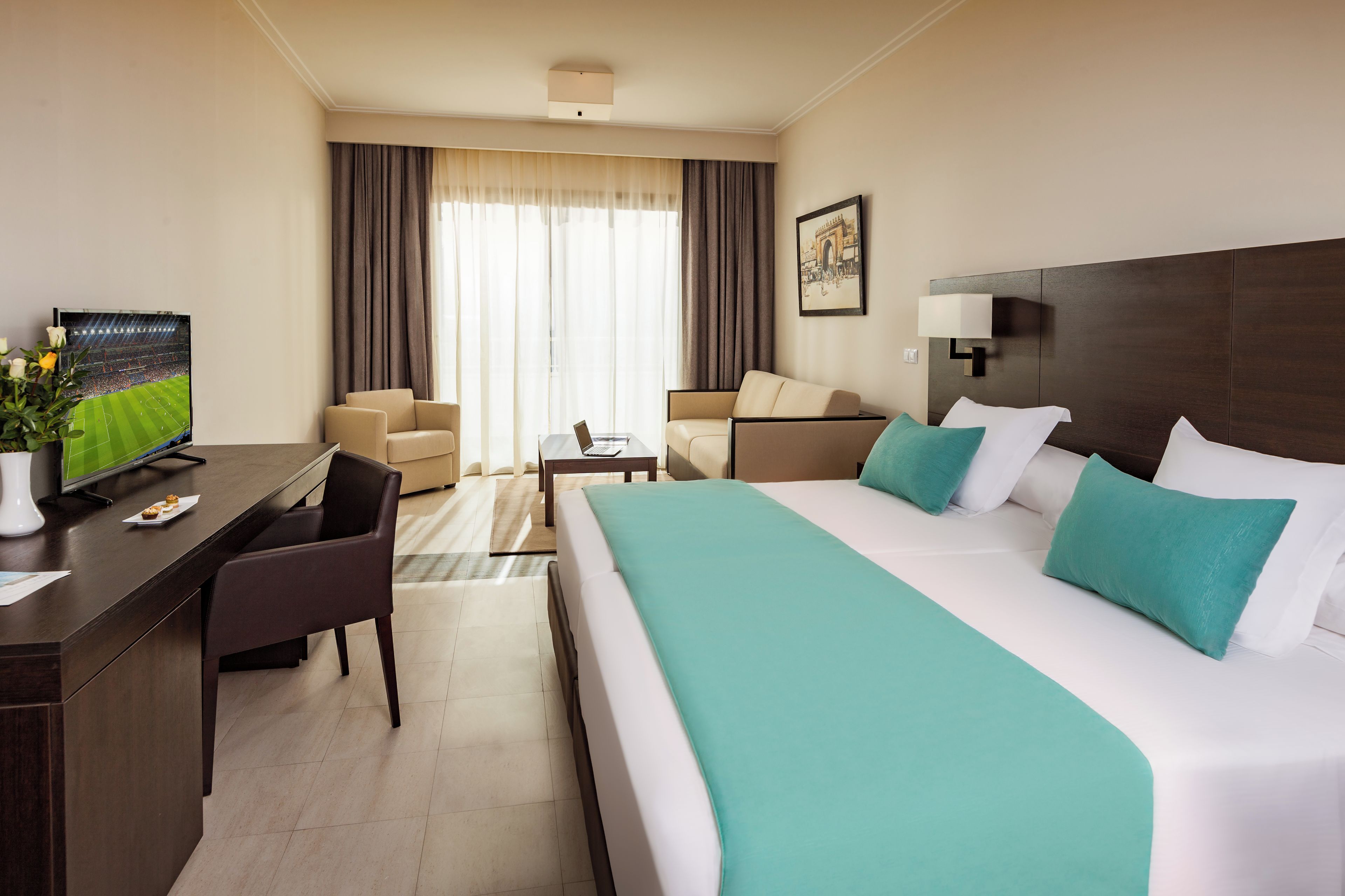 A hotel room with a large bed, a desk with a television, a sofa, and a coffee table.