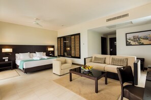 Une chambre d’hôtel avec un lit, deux canapés, une table basse avec des fruits et un tableau au mur.