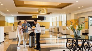 Un vestíbulo de hotel con una recepción, zonas de estar y una mesa de cristal con jarrones.