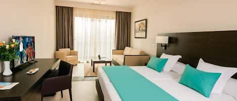 A hotel room with a bed, desk, chairs, and a painting on the wall.