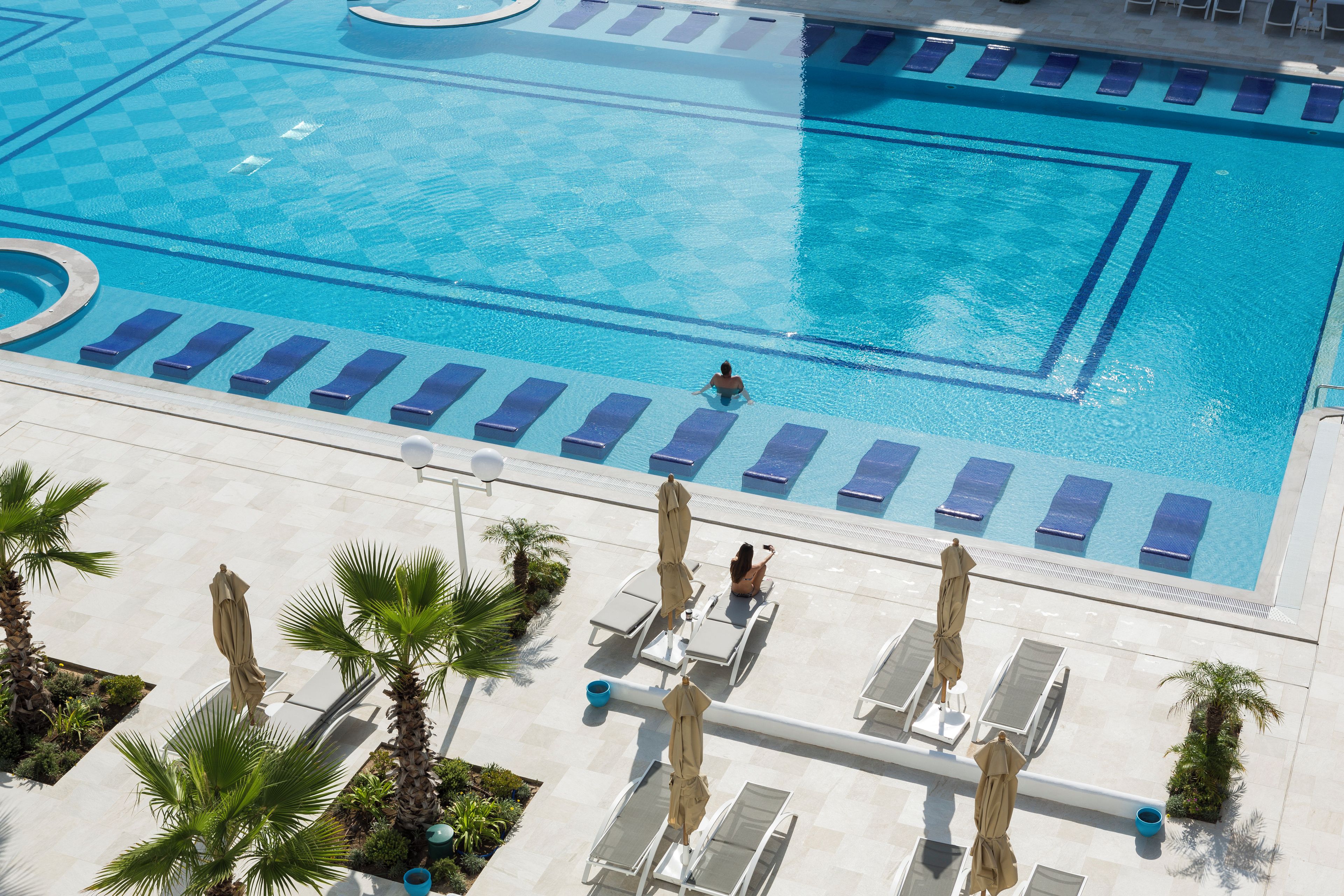 A large swimming pool with multiple lanes, sun loungers, and palm trees.