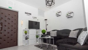 Ett modernt vardagsrum med en svart soffa, en vit hyllsektion och en platt-TV.
