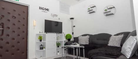 A modern living room with a black sofa, white shelving unit, and a flat-screen TV.