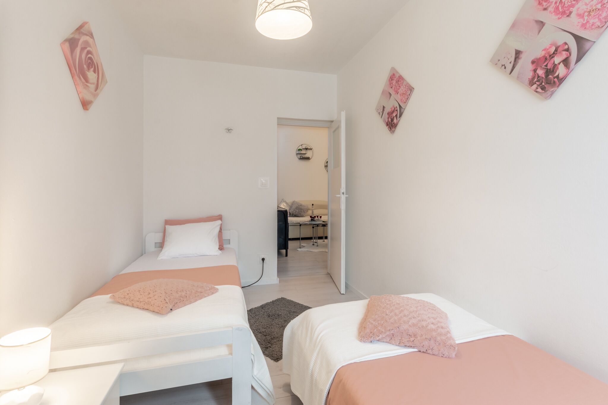 A bedroom with two beds, a small table, and a chair. There is a door leading to a bathroom and a hallway.