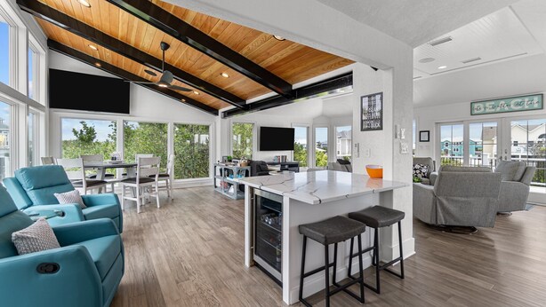 A spacious living area with a kitchen island, large windows, and a high ceiling with exposed beams.