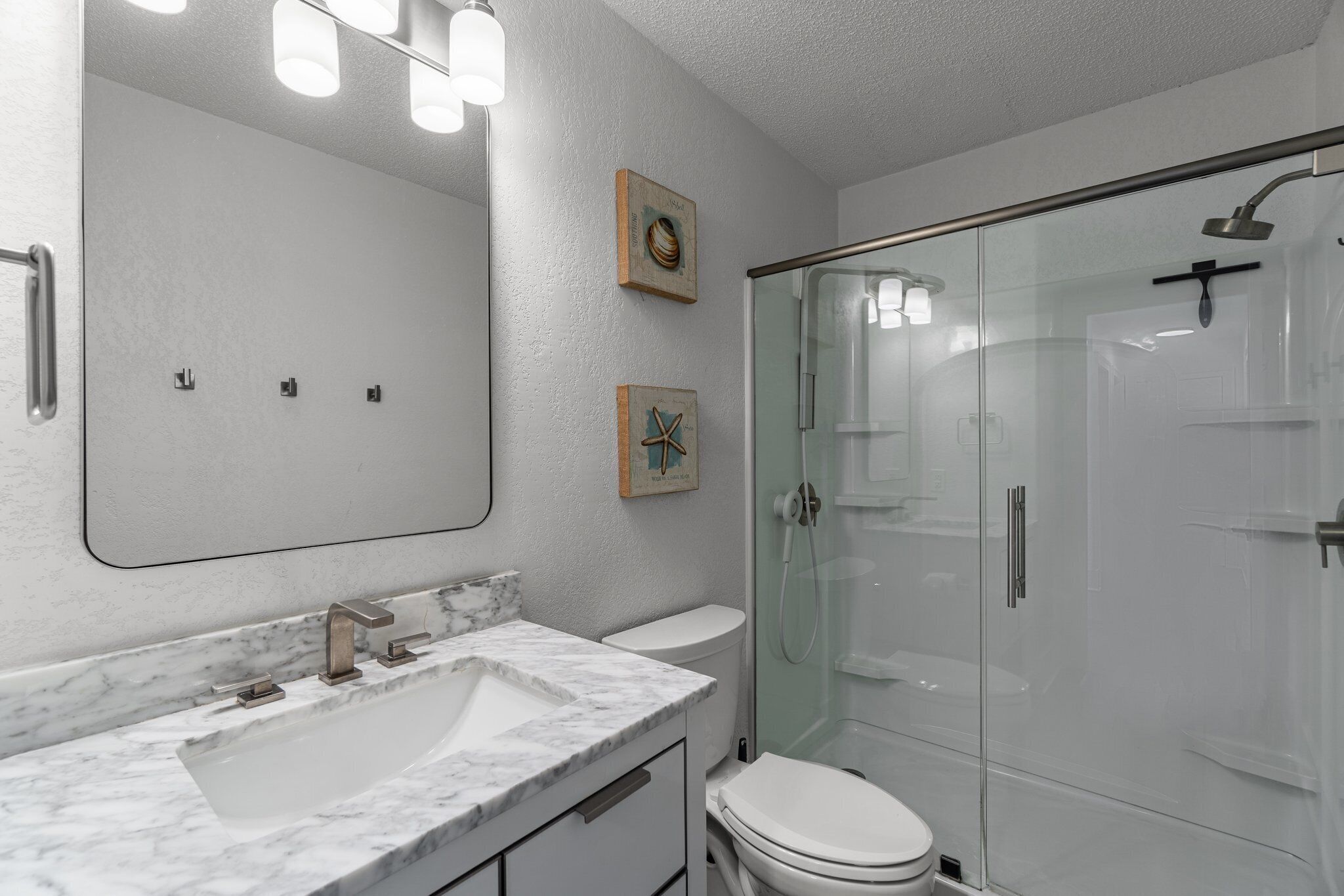 A modern bathroom with a glass-enclosed shower, a white sink with a marble countertop, and a toilet.