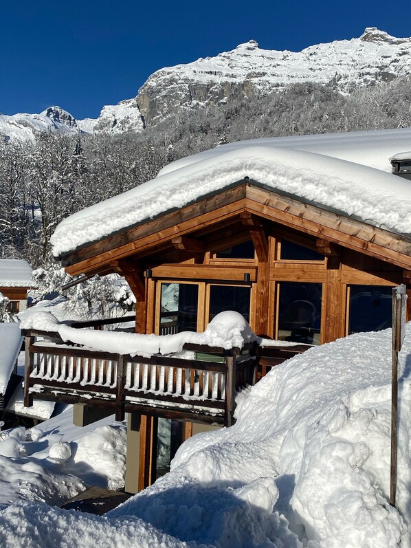 Un chalet en bois, dont le toit est recouvert de neige, et qui est entouré de neige.