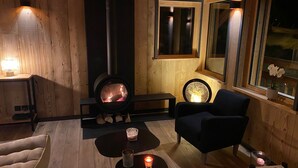 A cozy room with a wood-burning stove, a comfortable chair, a small table with candles, and a window with a view of the night sky. - Chalet Mélèze Vallée de Chamonix (Servoz)
