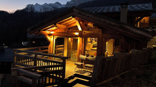 A wooden cabin with a deck and a large window, surrounded by mountains. - Chalet Mélèze Vallée de Chamonix (Servoz)