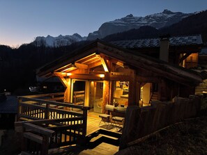 Une cabane en bois dotée d’une terrasse et d’une grande fenêtre, entourée de montagnes.
