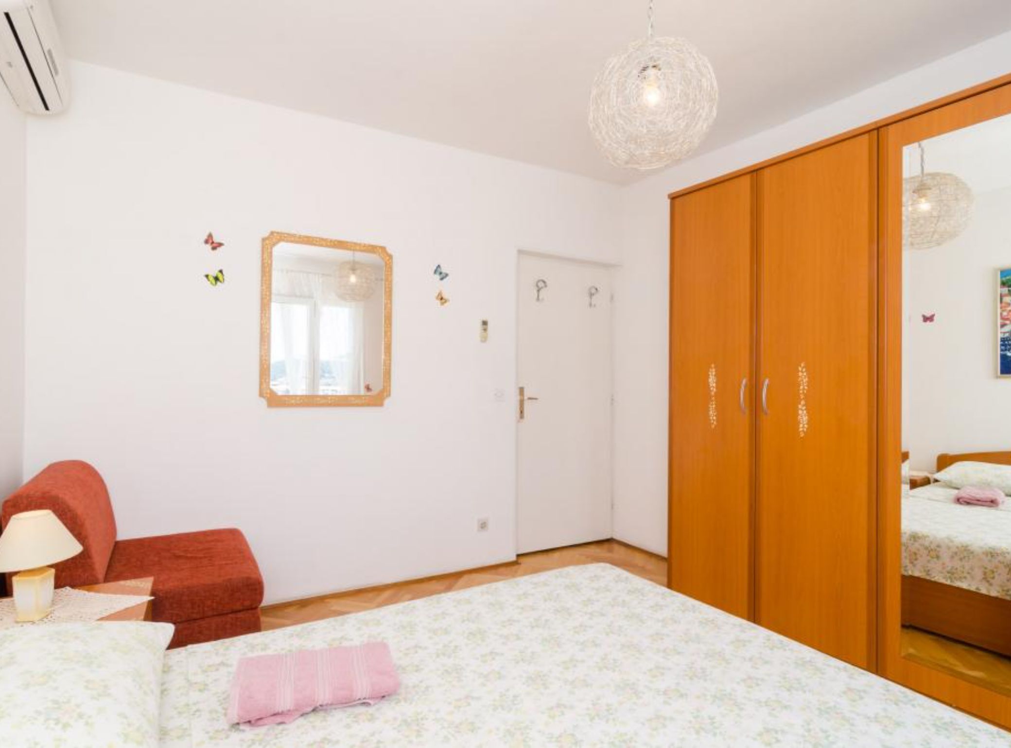 A bedroom with a bed, a wardrobe, a mirror, and a hanging light fixture.