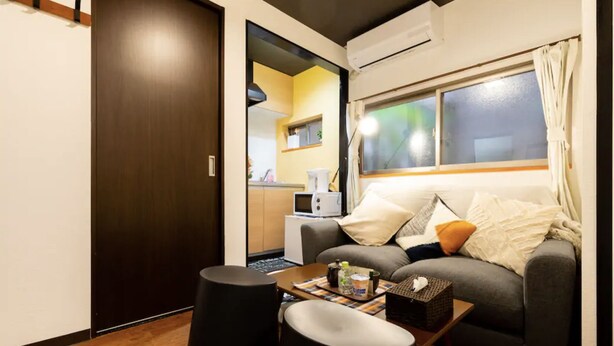 A compact living space with a sofa, a small table, and a kitchen area visible through an open door. - Tokinosyukudaikokucyou 1F (Osaka)