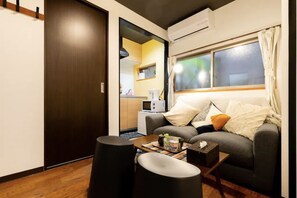 A compact living space with a sofa, a small table, and a kitchen area visible through an open door. - Tokinosyukudaikokucyou 1F (Osaka)