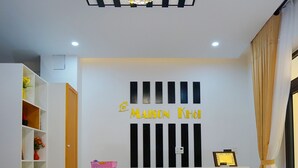 Un mostrador de recepción con una araña, un letrero que dice "MAISON KHÔI" y una estantería con diversos objetos.