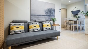 Een moderne woonkamer met een grijze bank, een eettafel met stoelen en een groot abstract schilderij aan de muur.