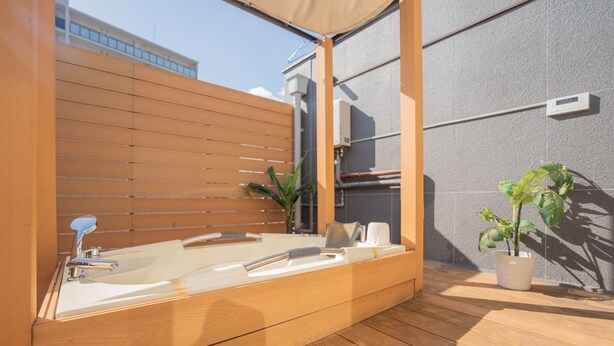 Een moderne, openlucht badkamer met een houten terras, een ruime badkuip en een potplant.