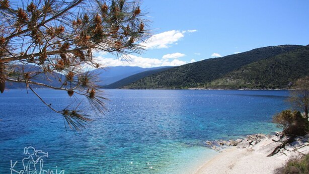 A clear view of a beach with a sandy shore, calm water, and a mountainous backdrop. - Villa Ianthi, Stamoulis villas at the heart of the island (Kefalonia)