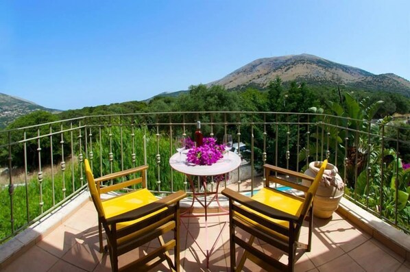 Un balcon avec deux chaises jaunes et une table, entouré d’une rambarde en métal, d’où l’on peut admirer un paysage montagneux.