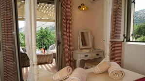 A bedroom with a bed, a bedside table with a mirror, and a view of the outdoors through a sliding door. - Villa Ianthi, Stamoulis villas at the heart of the island (Kefalonia)