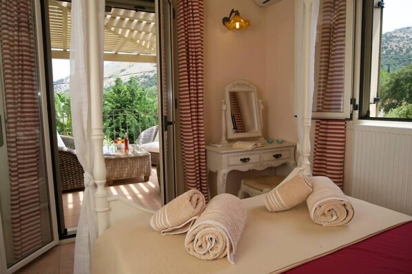 A bedroom with a bed, a bedside table with a mirror, and a view of the outdoors through a sliding door. - Villa Ianthi, Stamoulis villas at the heart of the island (Kefalonia)