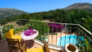 A balcony with yellow chairs and a table, a swimming pool, and a view of a mountain and greenery. - Villa Ianthi, Stamoulis villas at the heart of the island (Kefalonia)