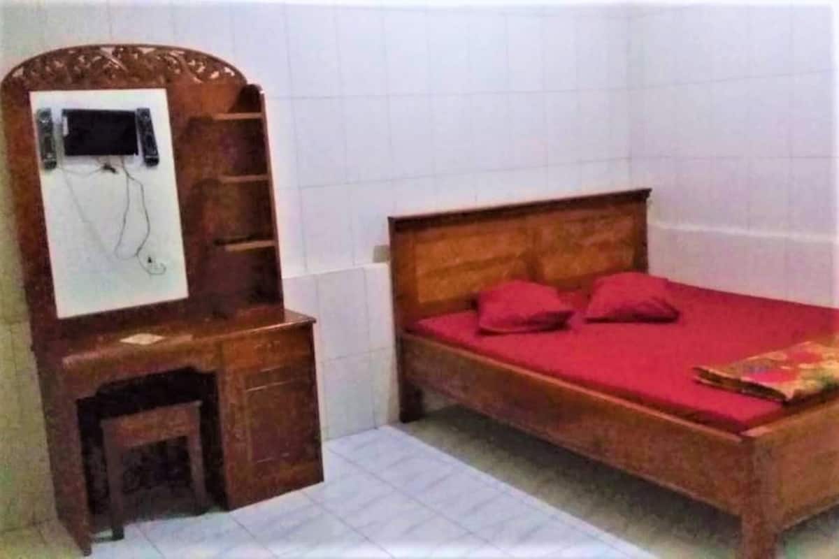 Ein Schlafzimmer mit einem hölzernen Bett, roter Bettwäsche, einem kleinen Holztisch und einem Spiegel.