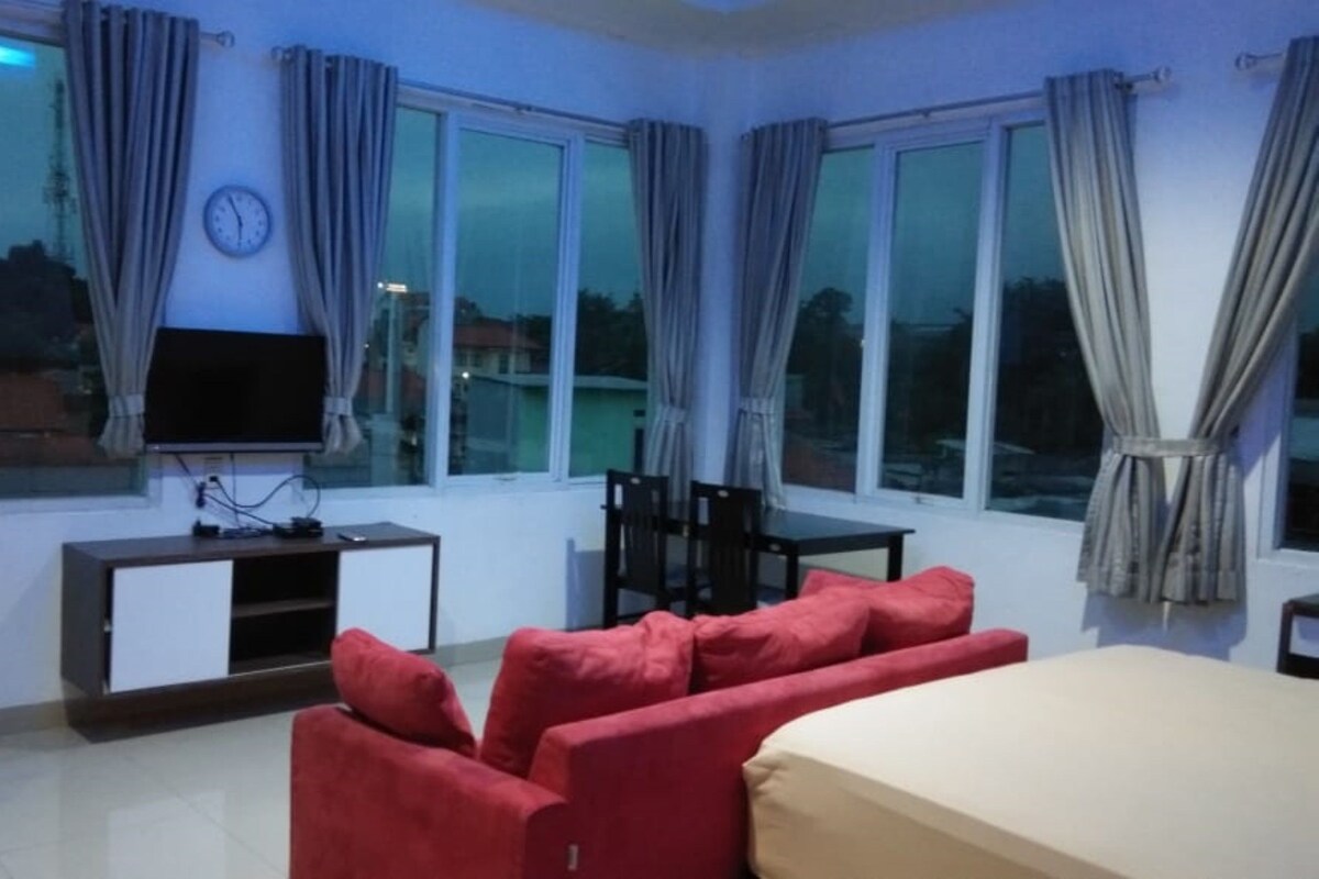 A room with a TV on a stand, a sofa, a table, and curtains on large windows.