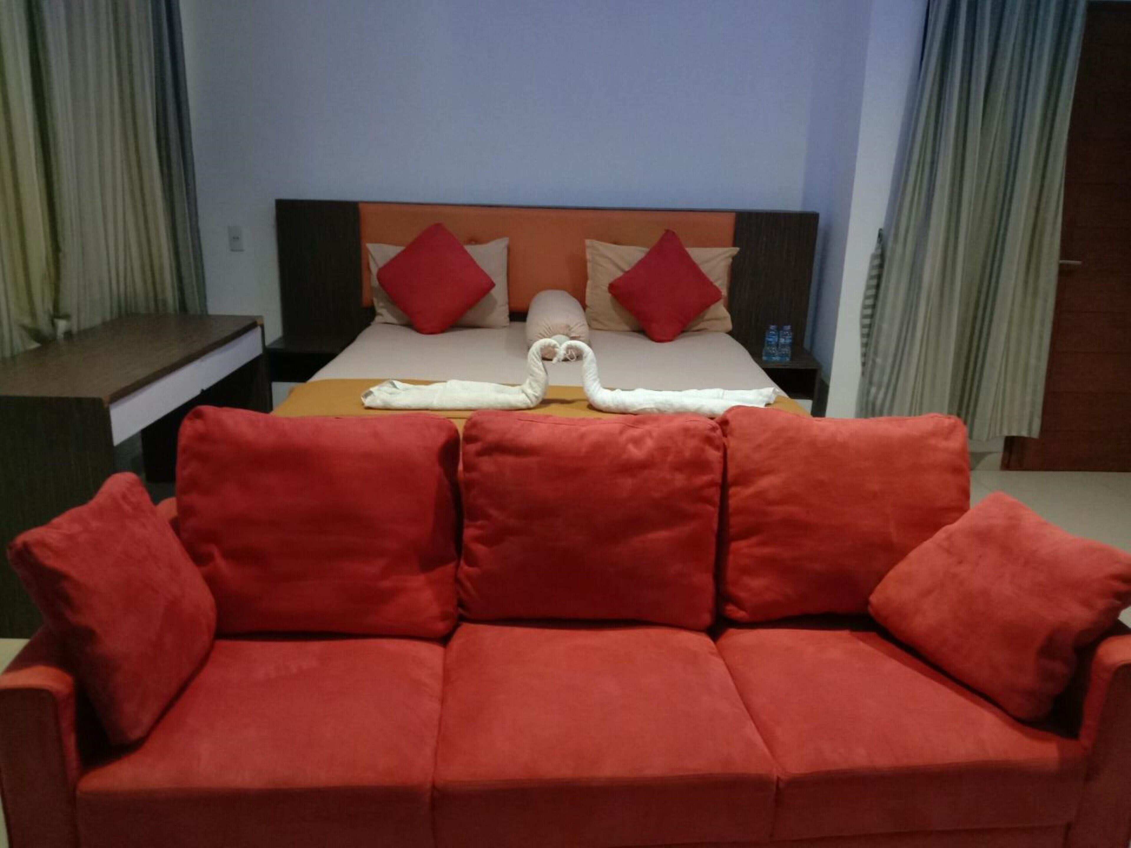 A hotel room with a bed, a red sofa, and a headboard with red and beige pillows.