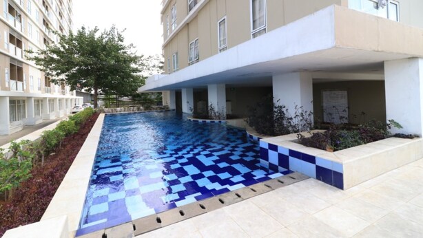 Ein Swimmingpool mit blau-kariertem Muster, umgeben von einer niedrigen Mauer und einem Gebäude mit Balkonen.