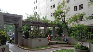 A courtyard with a covered seating area, surrounded by greenery and a multi-story building in the background. - Sewaunitkalcit (Jakarta)